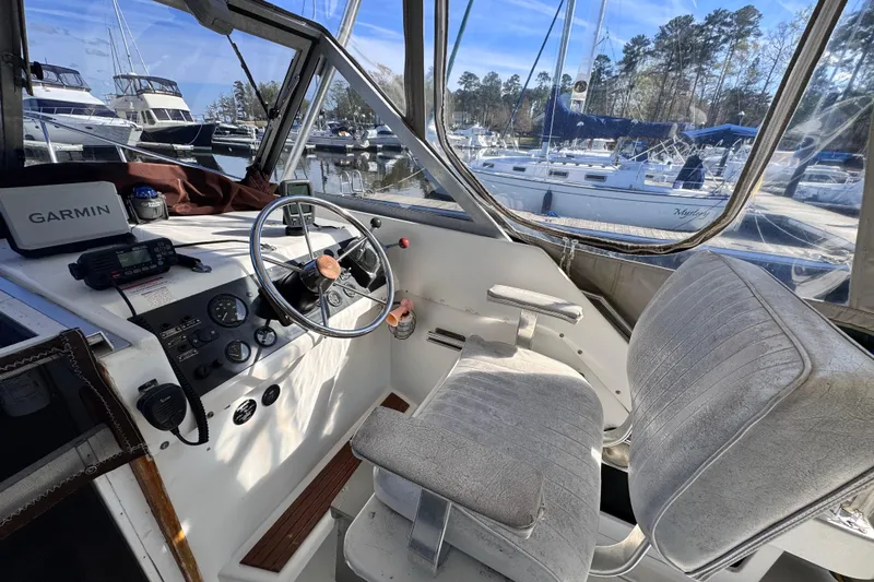 Slide: The Image of 1987 Luhrs Alura 30 boat cockpit with steering wheel, Garmin device, and marina view. - 12