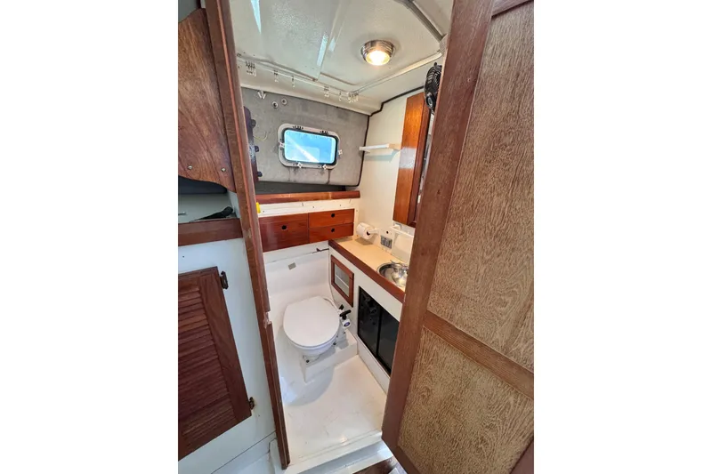 Slide: The Image of 1987 Luhrs Alura 30 boat bathroom with wooden cabinets and a small window. - 51