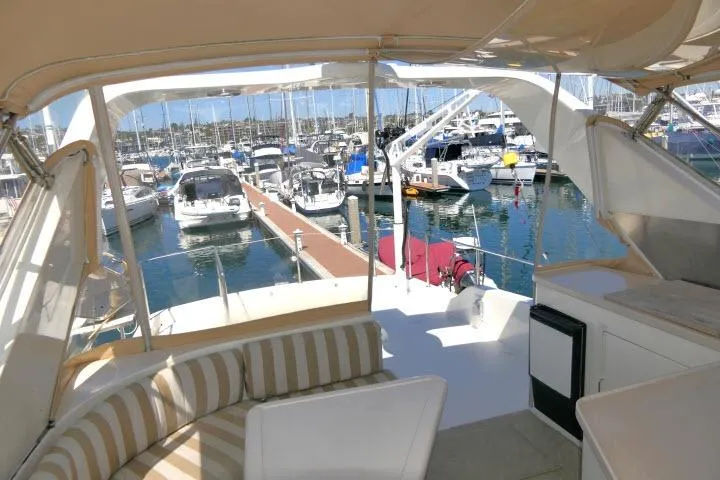 Slide: The Image of 1999 Hampton 490 Pilothouse yacht interior with marina view, featuring striped seating and docked boats. - 54