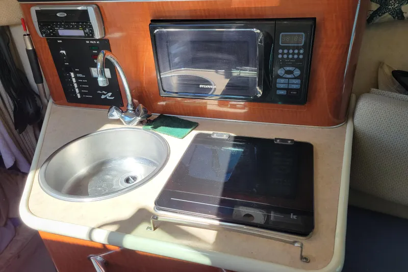Slide: The Image of 2004 Sea Ray 240 Sundancer kitchenette with sink, microwave, and stove. - 21