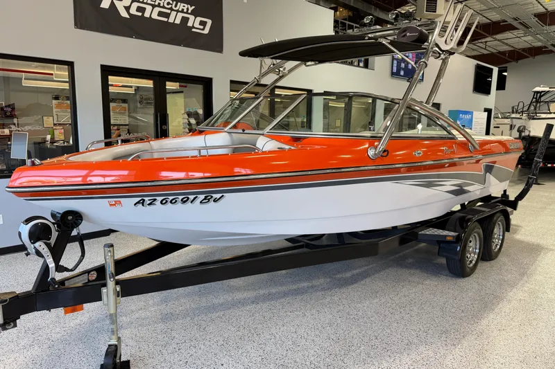 The Image of 2005 Calabria PRO V boat with vibrant orange and white design on a trailer indoors. - 0