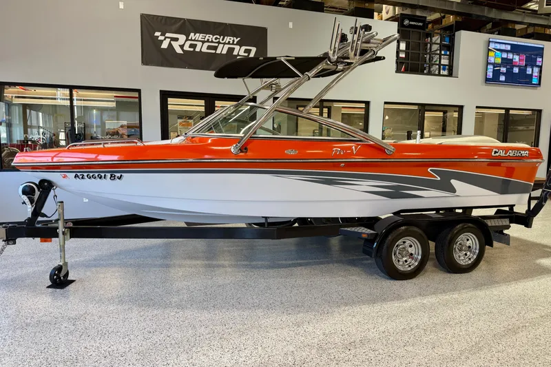 Slide: The Image of 2005 Calabria PRO V boat with vibrant orange and white design on a trailer indoors. - 3
