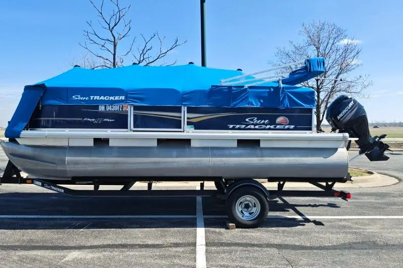 Slide: The Image of 2020 SUNTRACKER pb18 pontoon boat with blue cover on trailer in parking lot. - 8