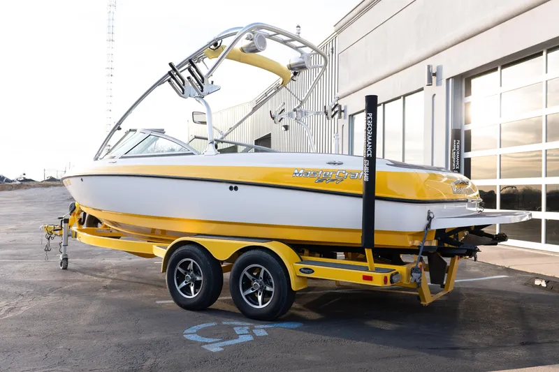 Slide: The Image of 2005 MasterCraft X10 boat in yellow and white on a trailer outside a building. - 3