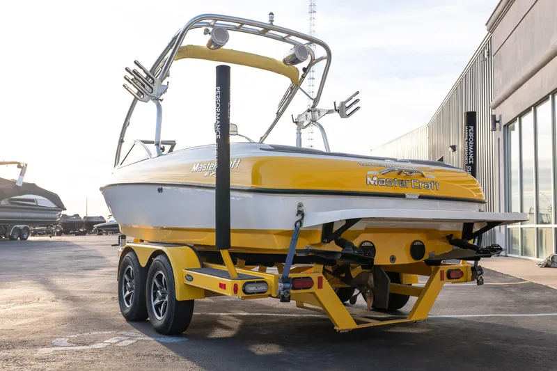 Slide: The Image of Yellow 2005 MasterCraft X10 boat on trailer, parked near a building. - 4