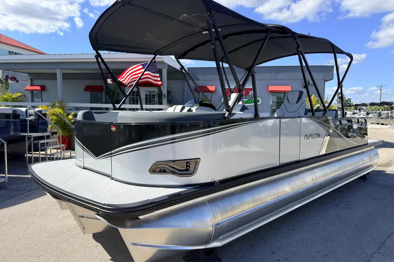 The Image of 2026 Avalon 2385 LSZ Versatile Rear Bench Tri Toon boat with canopy, parked outdoors. - 1