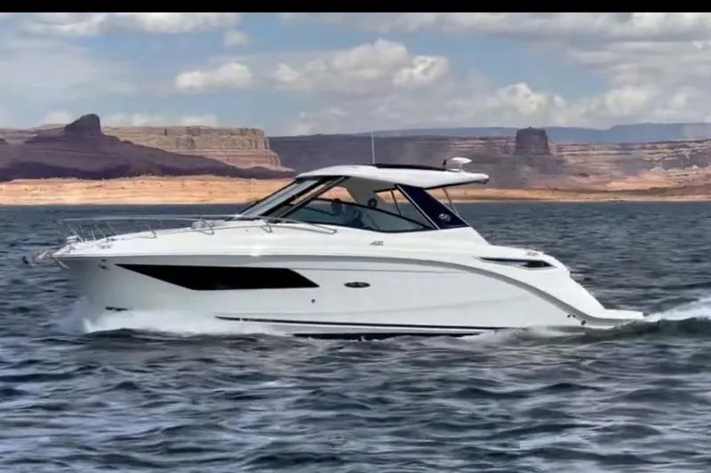 The Image of 2023 Sea Ray Sundancer 320 Coupe cruising on a scenic lake with rocky cliffs. - 0