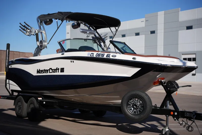 Slide: The Image of 2019 MasterCraft XT22 boat on trailer, parked outdoors near a modern building. - 13