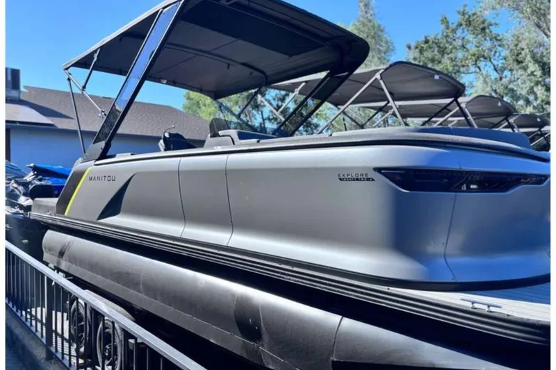 The Image of 2025 Manitou Explore pontoon boat with sleek design and canopy, parked outdoors. - 0