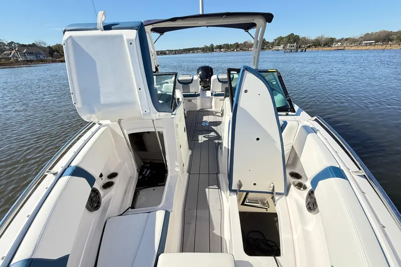 Slide: The Image of 2023 Chaparral 250 OSX boat interior with open storage compartments on a calm lake. - 18