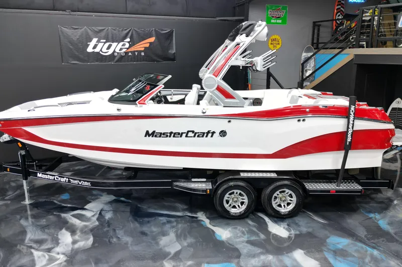 The Image of 2022 MasterCraft X24 boat in showroom, red and white design on trailer. - 1