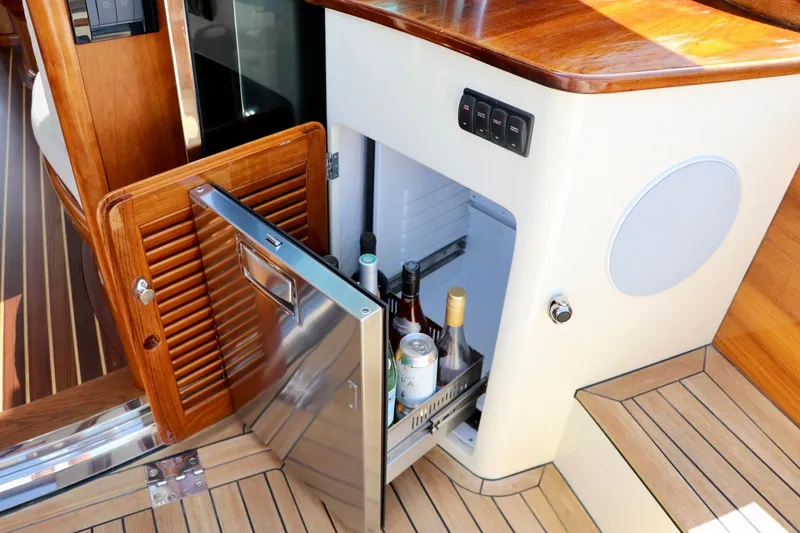Slide: The Image of Hinckley Talaria 48 MKII 2026 yacht interior with open mini fridge and wooden cabinetry. - 8