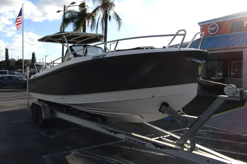 Slide: The Image of 2023 Windy SR28 CC boat on trailer, parked outdoors near palm trees and American flag. - 3