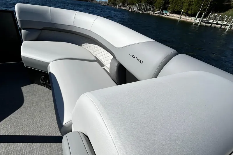 Slide: The Image of 2025 Lowe SS230WT boat with sleek white seating, docked by a serene lake. - 6