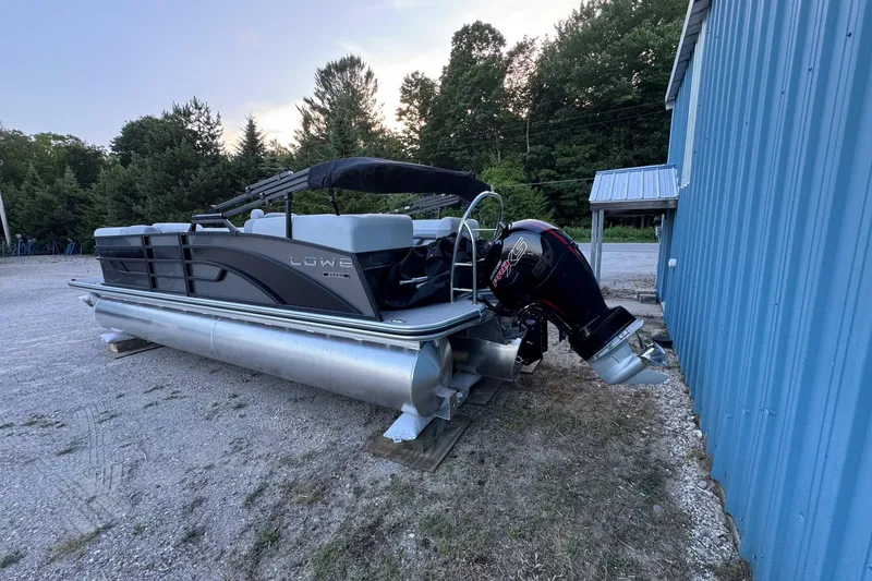 Slide: The Image of 2025 Lowe SS230WV pontoon boat parked beside a blue building. - 2