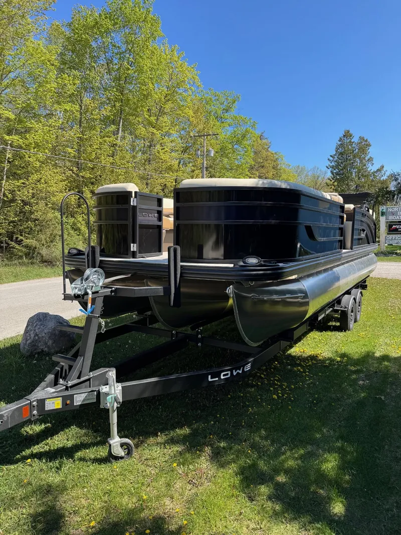 The Image of 2025 Lowe SS250WT pontoon boat on trailer, parked on grass with trees in background. - 0