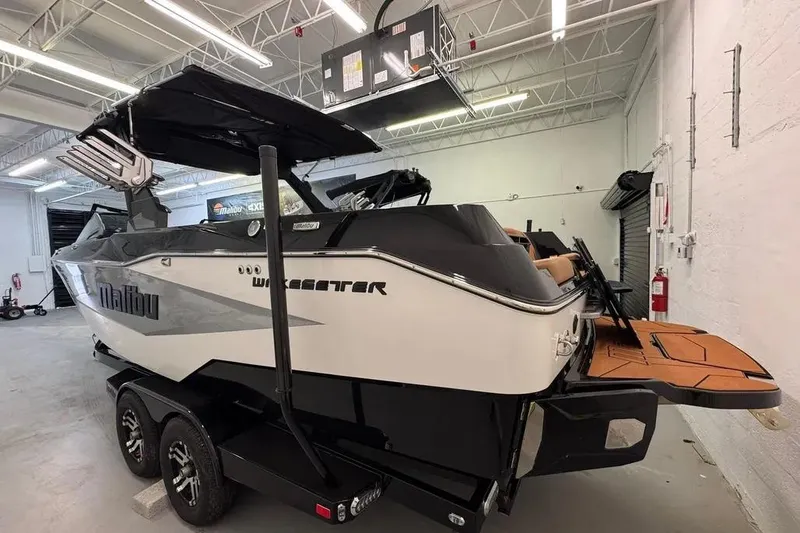 Slide: The Image of 2026 Malibu Wakesetter 25 LSV boat in a showroom, featuring sleek design and dual-axle trailer. - 2