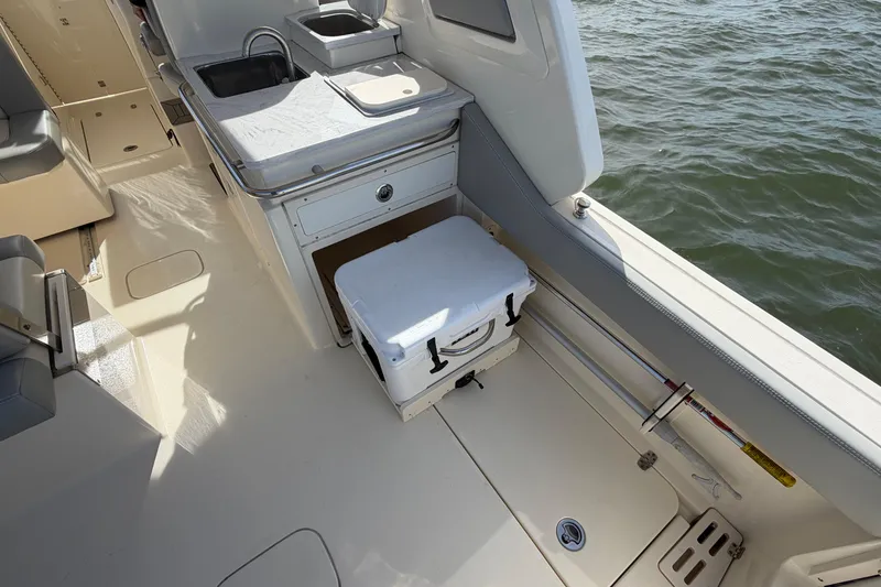 Slide: The Image of 2023 Scout 277 Dorado boat interior with sink, storage, and cooler by the water. - 17