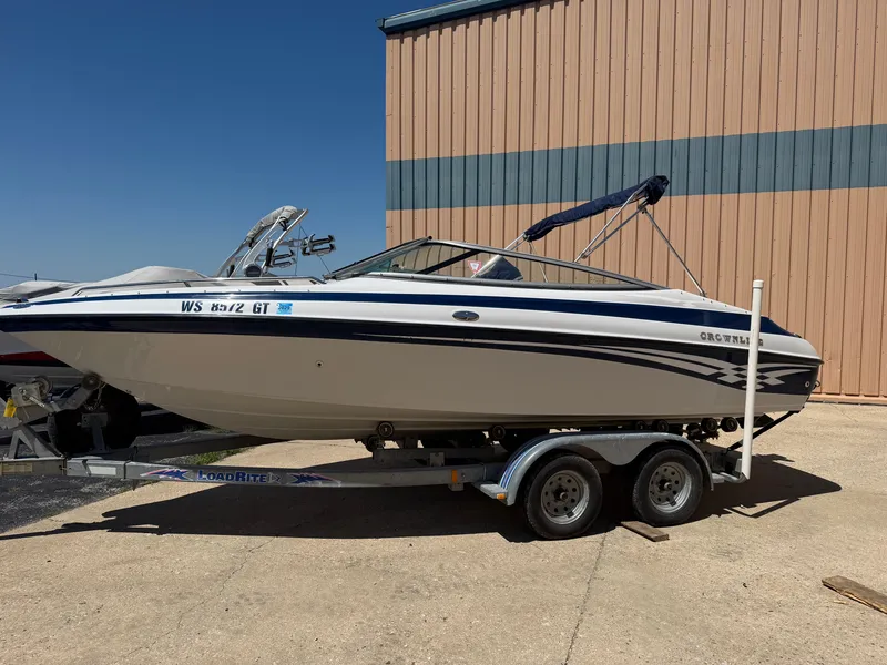 The Image of A 2002 Crownline 202 BR boat on a trailer, parked beside a building. - 0