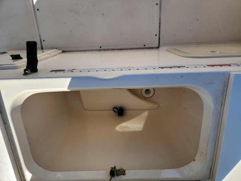 Slide: The Image of 2004 Pursuit 2470 Center Console boat storage compartment, open and empty, with visible drainage hole. - 5