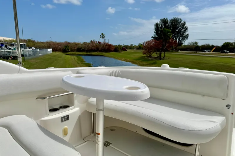 Slide: The Image of 2007 Larson Cabrio 274 boat interior with white seating and table, near a scenic waterway. - 24