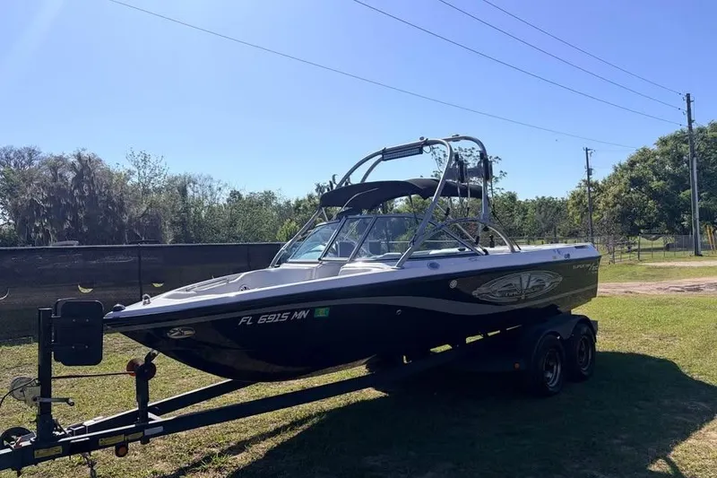 The Image of 2005 Nautique Super Air Nautique 210 boat on trailer, parked on grass. - 0