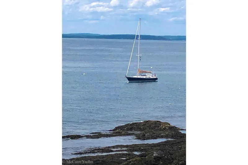 Slide: The Image of Sailboat Alden 43 Aft Cockpit, 1993 model, anchored in calm sea near rocky shore. - 68