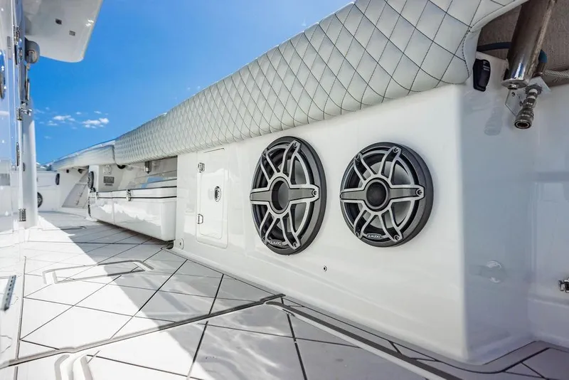 Slide: The Image of 2023 HCB 53 Suenos boat interior with speakers and quilted seating under blue sky. - 21