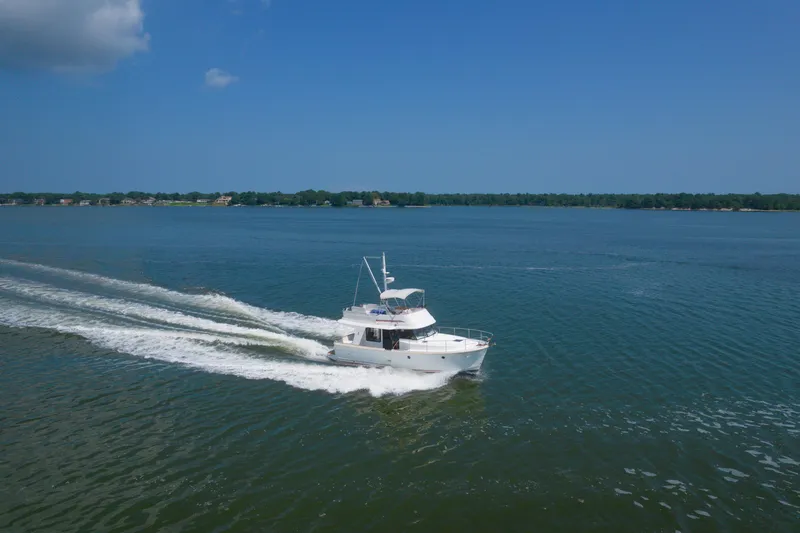 The Image of 2014 Beneteau Swift Trawler 34 cruising on a serene lake under a clear blue sky. - 1