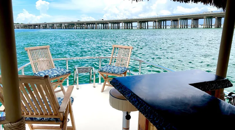Slide: The Image of 2023 Beachcat 23 Catamaran with chairs and table overlooking serene water and bridge. - 9