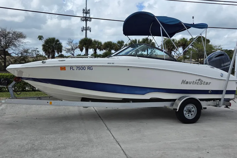 The Image of 2017 NauticStar 203DC Sport Deck boat on trailer with blue canopy. - 0