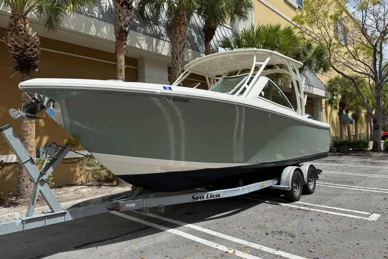 The Image of 2018 Sailfish 275 DC boat on trailer, parked near palm trees. - 0