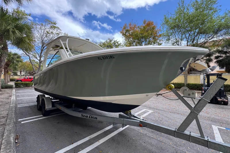 Slide: The Image of 2018 Sailfish 275 DC boat on trailer in parking lot, surrounded by trees. - 3