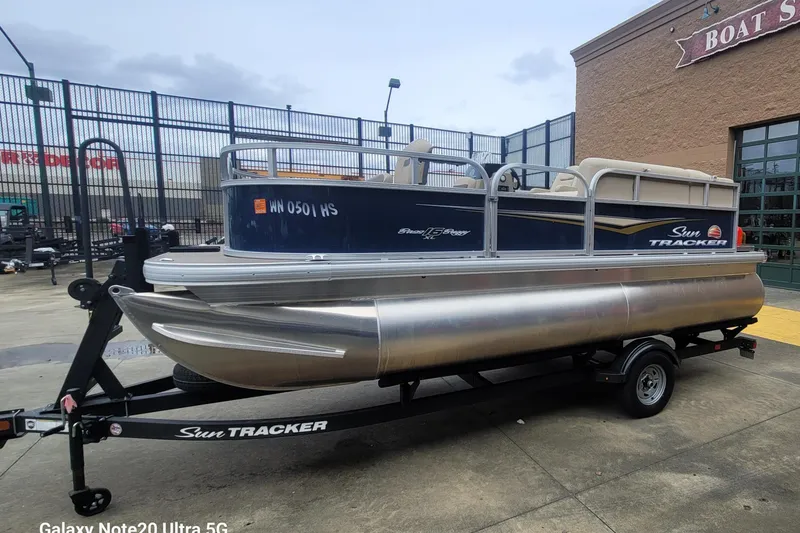 Slide: The Image of 2025 Sun Tracker Bass Buggy 16 XL pontoon boat on trailer outside a boat store. - 3