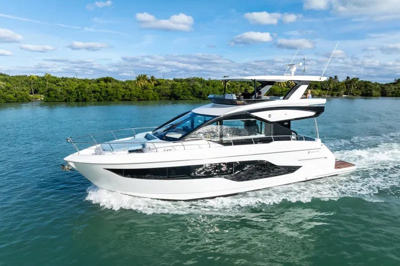 Slide: The Image of 2026 Cruisers Yachts 50 Fly cruising on a serene waterway under a clear blue sky. - 23