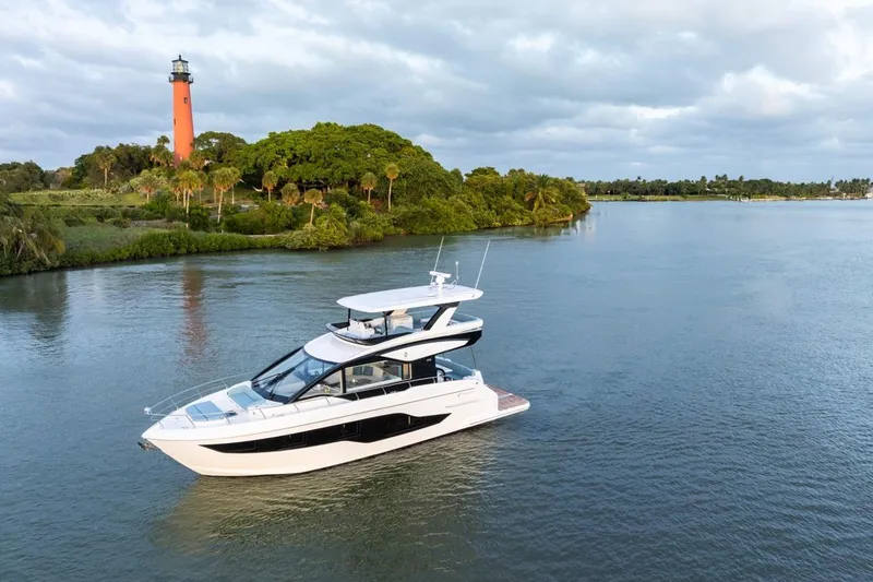 Slide: The Image of 2026 Cruisers Yachts 50 Fly on serene water near a lighthouse and lush greenery. - 41