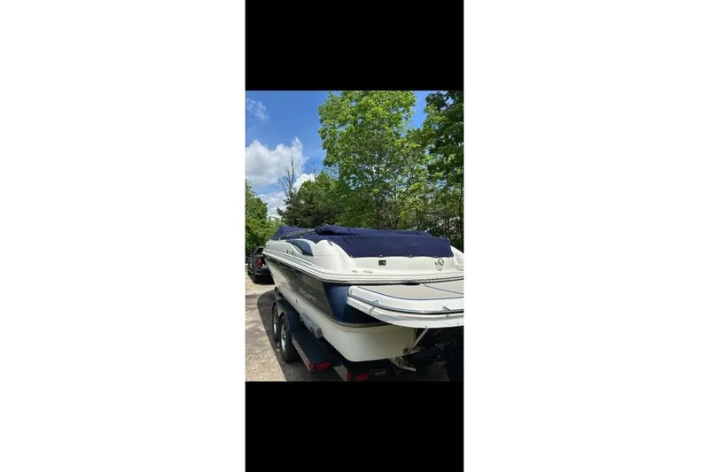 Slide: The Image of 2007 Bryant 270 boat with blue cover, parked on a trailer, surrounded by trees. - 30