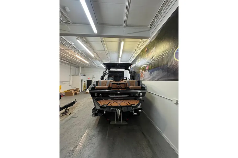Slide: The Image of 2026 Malibu M230 boat in a showroom, rear view with sleek design. - 2