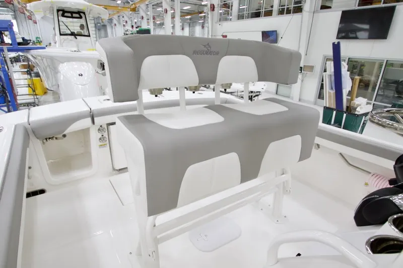 Slide: The Image of 2026 Regulator 23 boat interior with gray and white seating in a manufacturing facility. - 14