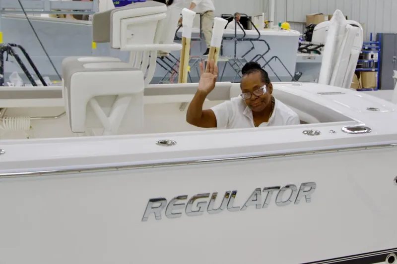 Slide: The Image of Person waving from a 2026 Regulator 23 boat in a workshop setting. - 22