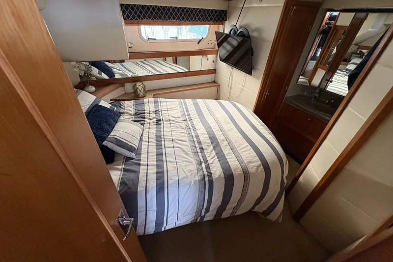 Slide: The Image of 1988 Bayliner 3587 Motoryacht bedroom with striped bedding and wall-mounted TV. - 87