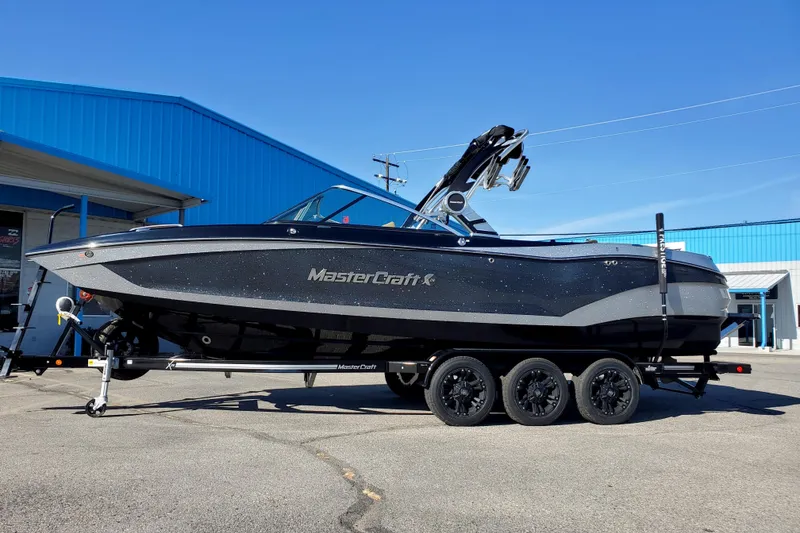 The Image of 2021 MasterCraft X26 boat on trailer, parked outside blue building. - 0
