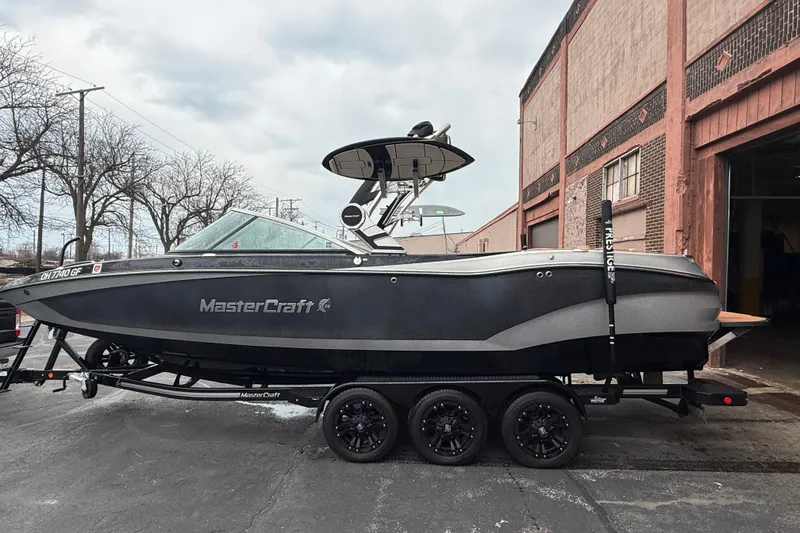 Slide: The Image of 2021 MasterCraft X26 boat on trailer, parked outside a brick building. - 2