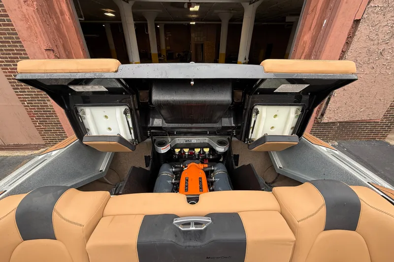 Slide: The Image of 2021 MasterCraft X26 boat engine compartment with tan seating and open storage compartments. - 29