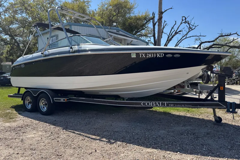 The Image of 2005 Cobalt 240 boat on trailer, parked outdoors under trees. - 0