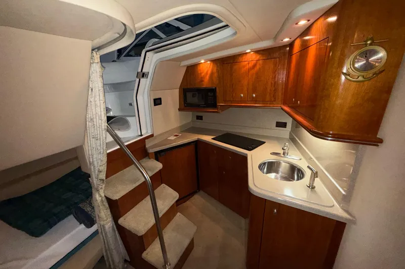 Slide: The Image of 2004 Cruisers Yachts 340 Express interior with kitchenette, wooden cabinets, and compact design. - 12