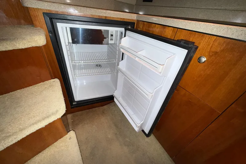 Slide: The Image of Open refrigerator inside 2004 Cruisers Yachts 340 Express, with wooden cabinetry and carpeted steps. - 17