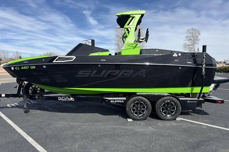 Slide: The Image of 2022 Supra SA 450 boat in black and green on a trailer, parked outdoors. - 2