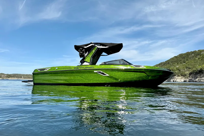 Slide: The Image of 2021 Centurion Ri245 boat in vibrant green on a serene lake under a clear blue sky. - 3