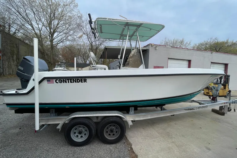 The Image of 1999 Contender 23 CC boat on trailer, parked outdoors near industrial building. - 1